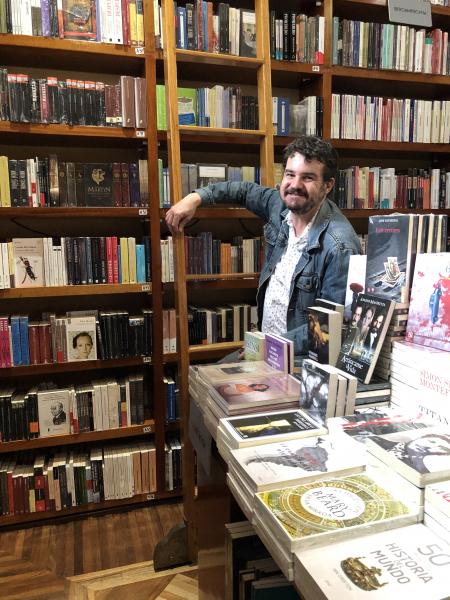 Daron Mueller in a bookstore leaning against a rolling bookshelf ladder